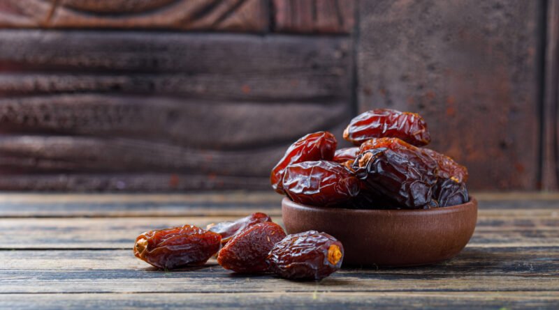 dates palm benefits.Sweet dates in a clay plate on stone tile and wooden background, side view.